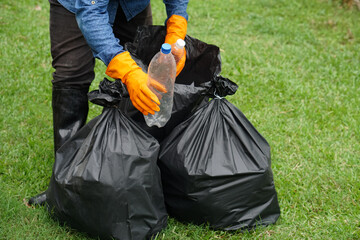 Closeup garbage collector worker hands hold plastic bottles to put into black garbage bags to...