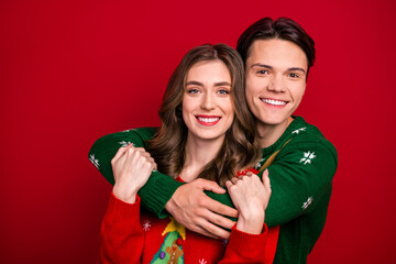 Photo of cheerful sweet brother sister wear xmas sweaters embracing empty space isolated red color background
