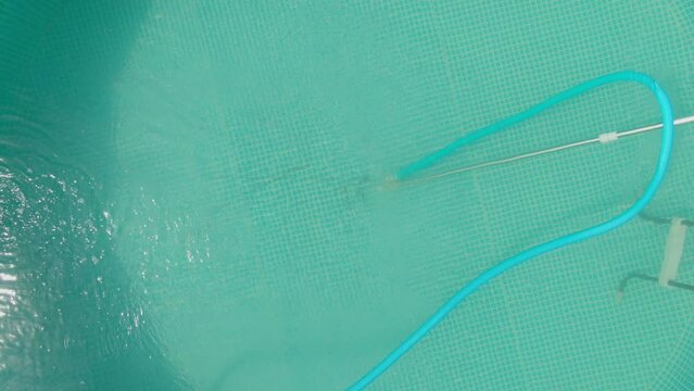Aerial view on the woman in a hat cleaning the pool with a water vacuum cleaner