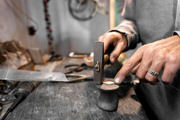 A craftsman jeweler is straightening a piece of metal using a hammer