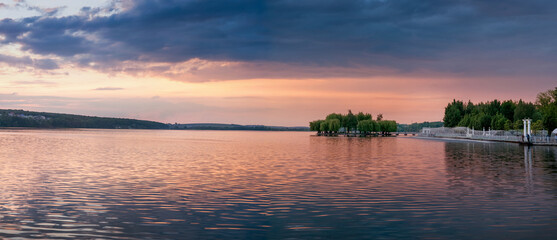 Panoramic view of beautiful lake, island with silhouette of trees under evening purple sky at sunset. Embankment of Ternopil, Ukraine.