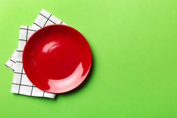 Top view on colored background empty round red plate on tablecloth for food. Empty dish on napkin with space for your design