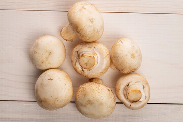 Several whole organic fresh mouth-watering champignon mushrooms, on a table made of natural wood, top view.