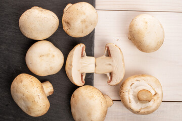 A few whole and two halves of organic fresh appetizing mushrooms champignon with a serving board of slate on a table made of white painted natural wood, top view.