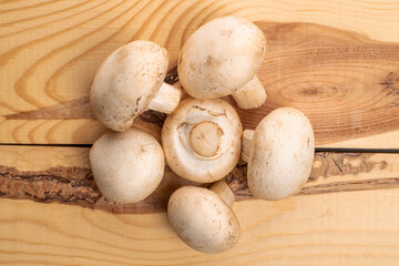 Several whole organic fresh mouth-watering champignon mushrooms, on a table made of natural wood, top view.