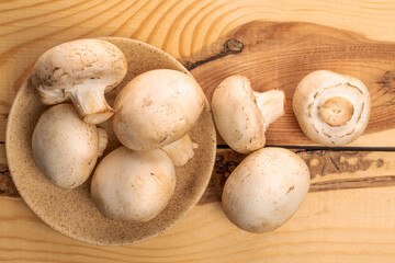 Several whole organic fresh appetizing mushrooms champignon with ceramic saucer, on a table made of wood, top view.