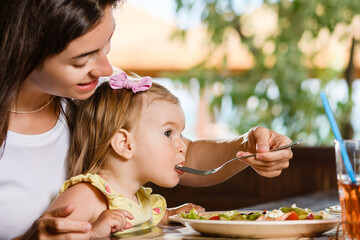 Woman mom feed toddler girl with salad