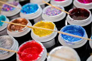 Samples of cosmetic makeup glitter with wooden stick in row on counter for sale in cosmetics shop,...