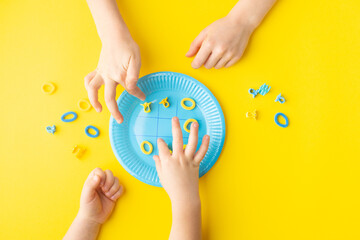 Playing noughts and crosses with hairpins on paper plate. Colorful concept. Minimalist concept.