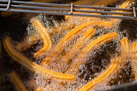 Process of cooking homemade crunchy yellow churros in boiling oil at summer outdoor food market - close up view. Traditional spanich cuisine, cookery, gastronomy, street food concept