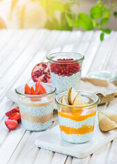 Breakfast chia desserts in jars with fresh fruit - pomegranate, pear and strawberry on a white, wooden board