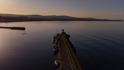 Drone photo of lighthouse at the end of pier in the warm sunset in Wicklow, Ireland 