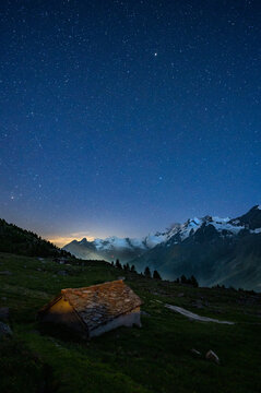 Old alpine hut with stone roof with stars above at night