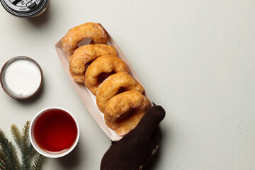 mittened hands hold a cardboard plate with donuts. Flatlay on a light background, with a hot drink and fir branches.