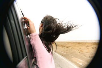 Fototapeta na wymiar Viento sopla cabello de mujer joven que sale por la ventana del auto en movimiento