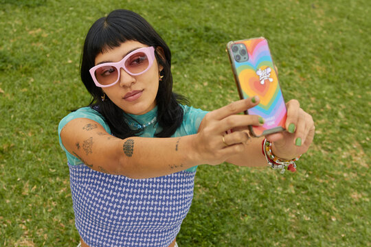 Mujer joven tatuada y con estilo se toma una selfie con su teléfono en el parque
