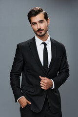 Stylish young man in a brunette business suit posing on a gray background and smiling businessman