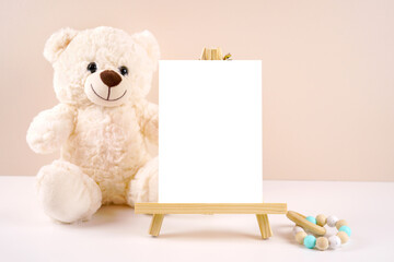 Table number easel with 5x7 card product mockup. Baby shower 1st birthday Christening gender neutral. Styled setting with white teddy bear against a beige and white background. Negative copy space.