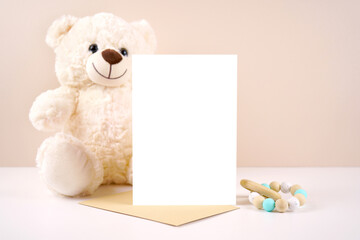 5x7 vertical greeting card party invitation product mockup. Baby shower birthday christening gender neutral. Styled with white teddy bear against a beige and white background. Negative copy space.