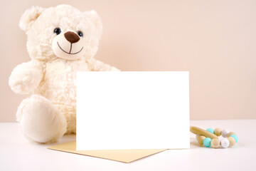 5x7 horizontal greeting card party invitation product mockup. Baby shower birthday christening gender neutral. Styled with white teddy bear against a beige and white background. Negative copy space.