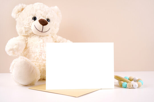 5x7 horizontal greeting card party invitation product mockup. Baby shower birthday christening gender neutral. Styled with white teddy bear against a beige and white background. Negative copy space.