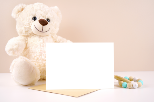 5x7 horizontal greeting card party invitation product mockup. Baby shower birthday christening gender neutral. Styled with white teddy bear against a beige and white background. Negative copy space.