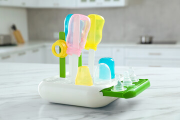 Dryer with baby bottles and nipples after sterilization on white marble table in kitchen
