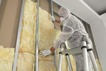 Worker insulating wall using ladder indoors, low angle view