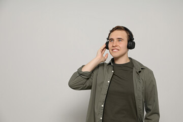 Handsome young man with headphones on light grey background. Space for text