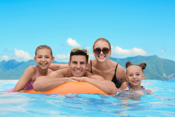 Obraz premium Happy family in outdoor swimming pool at luxury resort with beautiful view of mountains on sunny day