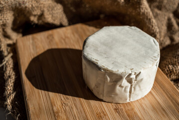 A composition of a round cheese head with white mold on a bamboo board on a background of burlap. Aesthetic serving of food