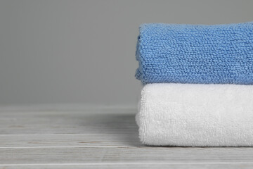 Fototapeta na wymiar Soft folded towels on white wooden table against light grey background, space for text