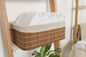 Fototapeta na wymiar Soft towels in wicker basket on decorative ladder near white wall
