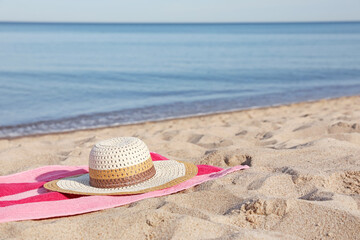 Beach towel and straw hat on sand near sea, space for text