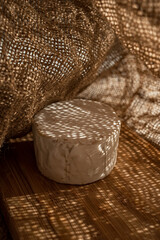 Composition of a round cheese head with white mold on a bamboo board with droplets of light penetrating through the burlap