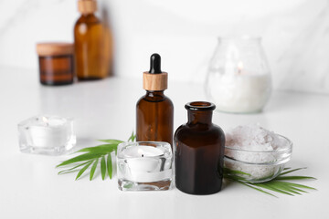 Obraz na płótnie Canvas Essential oils, sea salt and candles on white table in bathroom, closeup