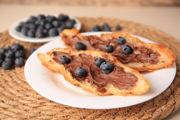 Tasty croissant with chocolate paste and blueberries on wicker mat