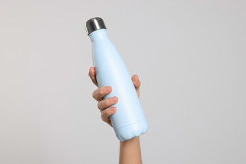 Woman holding thermo bottle of drink on light background, closeup