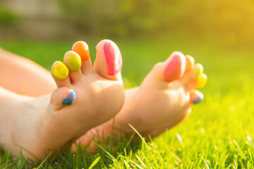Naklejka premium Teenage girl with painted toes on green grass outdoors, closeup