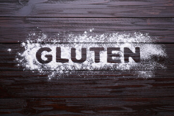 Word Gluten written with flour on dark wooden table, top view