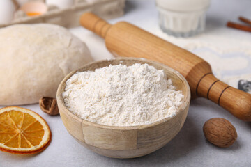 Fototapeta na wymiar Bowl of flour, rolling pin and ingredients on white table