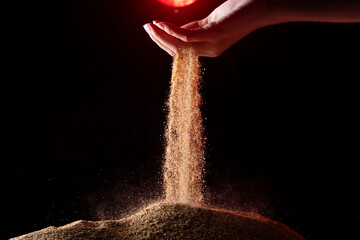 Hand releasing dropping sand. Fine Sand flowing pouring through fingers against black background....