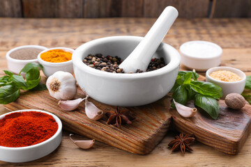 Mortar with pestle and different spices on wooden table