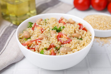 Delicious quinoa salad with tomatoes, beans and parsley served on white tiled table