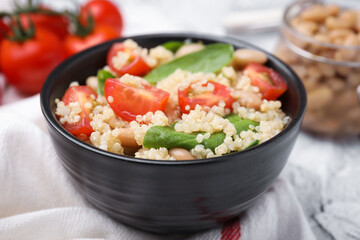 Delicious quinoa salad with tomatoes, beans and spinach leaves served on white table