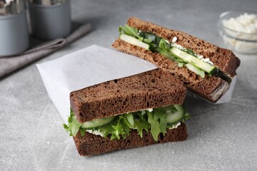 Tasty sandwiches with cream cheese, cucumber and greens on light grey table