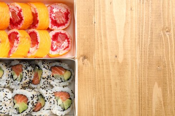Food delivery. Paper boxes with delicious sushi rolls on wooden table, flat lay and space for text