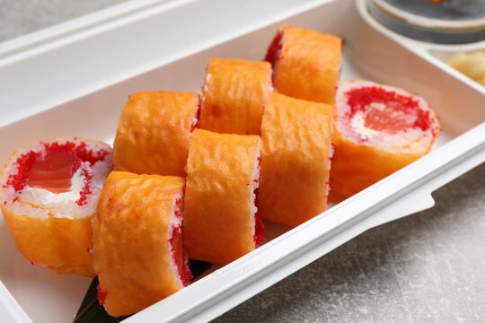 Delicious mamenori sushi rolls in plastic container on table, closeup. Food delivery