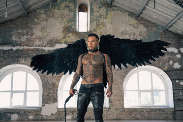 handsome man with wings.Male angel with black wings.  Muscular shirtless man with whip. Brutal handsome man with tattooed body. Muscular athletic sexy male 