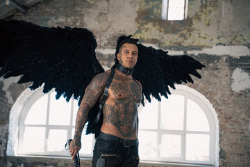 handsome man with wings.Male angel with black wings.  Muscular shirtless man with whip. Brutal handsome man with tattooed body. Muscular athletic sexy male 